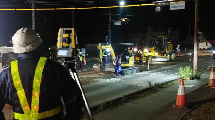 夜間の道路舗装工事で測量機器と施工機械を操作する作業員